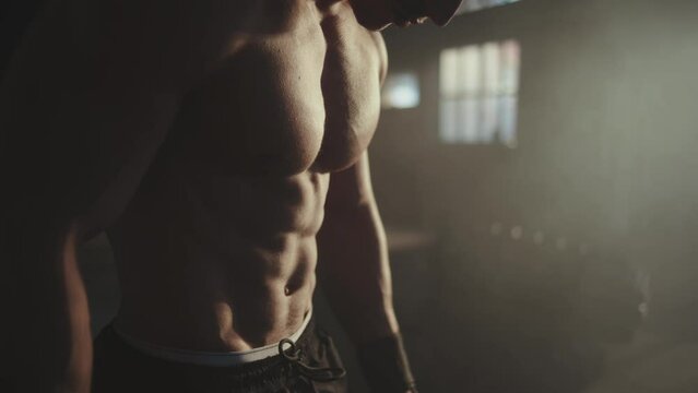 Close-up view of a fitness model displaying his large muscles at gym in the dark background. Camera movement
