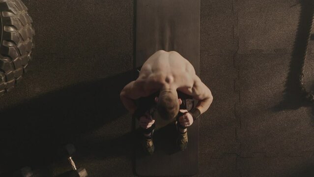 Top view of a shirtless muscular man doing sit-up exercise on the floor in the spors gym. Slow-motio shot