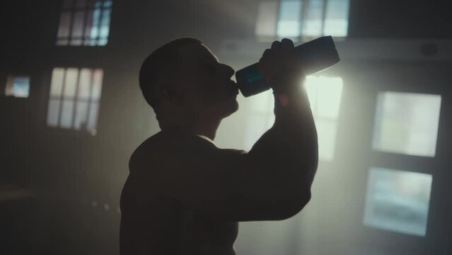 Slow-motion shot of a male athlete drinking water from bottle after hard workout in the gym