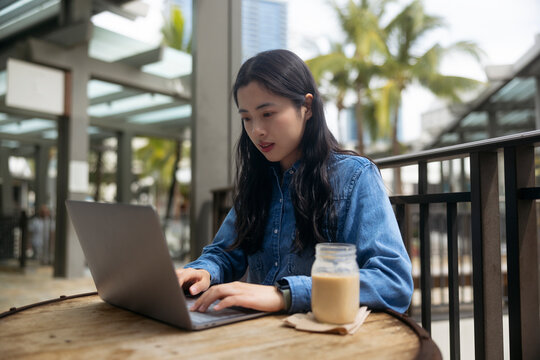 Portrait of a cute asian student girl coding IT laptop outdoors cafe and drinking a cup of coffee