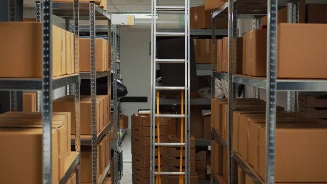 Small business warehouse in storage room filled with carton packs, office space with laptop for product inventory or logistics. Empty depot with stacks of merchandise for stock distribution.