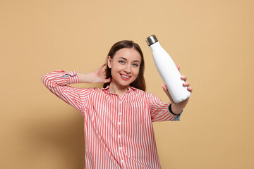 Beautiful young woman with thermos bottle on beige background
