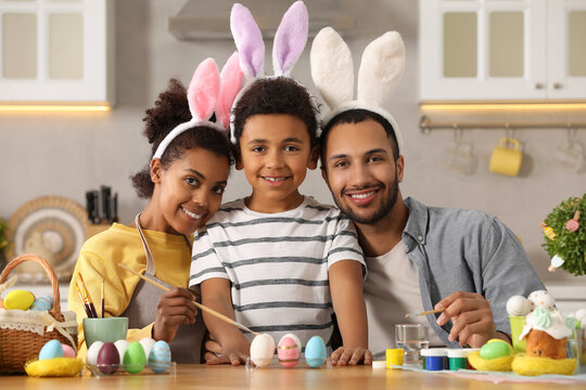 Happy African American family painting Easter eggs at table in kitchen