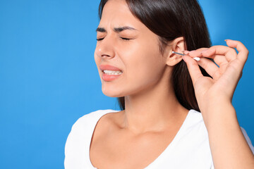 Young woman cleaning ear with cotton swab on light blue background, closeup