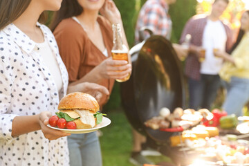 Group of friends having barbecue party outdoors, space for text. Focus on burger