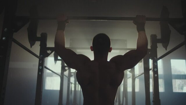 Back view of a handsome strong athletic men pumping up back muscles doing pull-ups exercises in gym