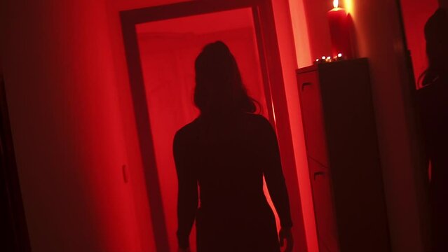 Black silhouette of a curvy woman walking with her back to the camera in a corridor with a red low light environment.