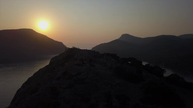 Aerial flyover: Tourists gather on mountain top to view ocean sunset