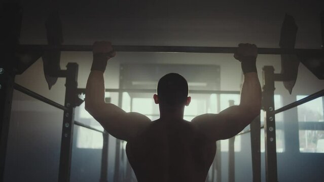 Slow-motion back view of a handsome strong athletic men pumping up back muscles doing pull-ups exercises in gym