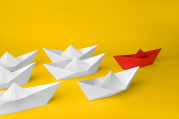 Group of paper boats following red one on yellow background. Leadership concept