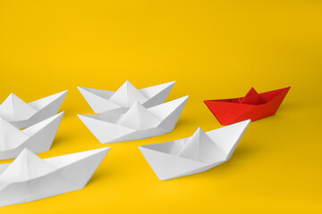 Obraz premium Group of paper boats following red one on yellow background. Leadership concept
