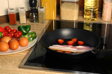 Cooking bacon with tomatoes in frying pan. Ingredients for breakfast