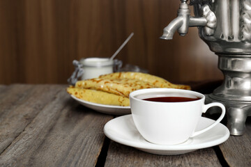 Vintage samovar, cup of hot drink and pancakes served on wooden table. Traditional Russian tea ceremony
