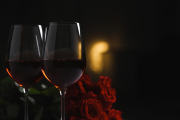 Glasses of red wine and rose flowers on blurred background, space for text. Romantic atmosphere