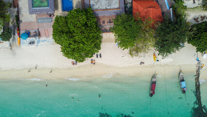 Aerial view of beautiful white sand beach and turquoise waters of Andaman Sea, Phi Phi, Krabi, Thailand. Entrance to a beach hotel, traditional longtail boats arriving. Vacation in Southeast Asia