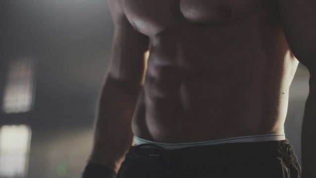 Unrecognizable muscular strong man with six pack abs posing on camera at gym. Close-up shot