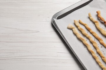 Baking sheet with homemade breadsticks on white wooden table, top view with space for text. Cooking traditional grissini