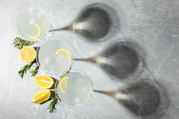 Martini glasses of refreshing cocktail decorated with lemon slices and rosemary on light grey textured table, flat lay. Space for text