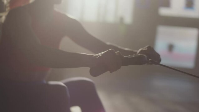 Slow-motion tracking shot of a fitness woman using rowing machine in the gym. Female doing cardio workout on rowing machine