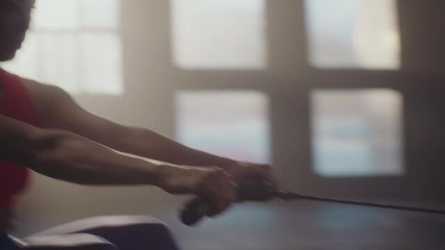 Slow-motion shot of a young athlete woman doing rowing exercises in dark concept gym
