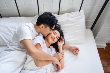 Obraz na płótnie Canvas Asian husband kissing his wife while lying down sleep on bed in bedroom