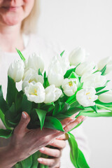 A bouquet of white tulips in the palms of a beautiful blonde Caucasian woman .