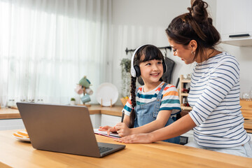 Caucasian young girl kid learning online class at home with mother. 