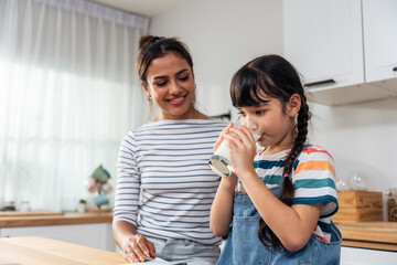 Caucasian little kid holding a cup of milk and drinking with mother. 