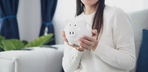 Young asian woman holding white piggy bank at home. Save money and investment concept