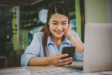 Business asian woman sitting at her desk with laptop using mobile phone during checking an email or social media on internet.