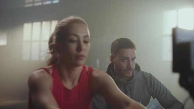 Slow-motion shot of a female athlete giving high five with her personal trainer after successful training on rowing machine