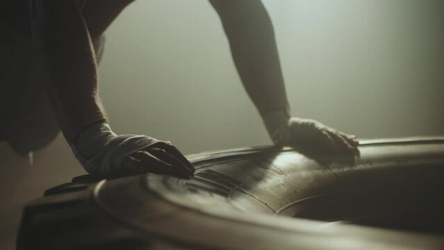 Close-up on hands of young shirtless mascular man preparing for push ups after wrapping his hands with boxing bandage on rubber tyre