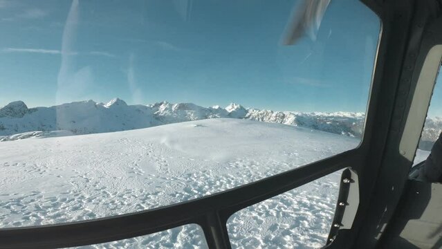 Wide angle backseat footage of a helicopter landing on top of a cold snowy winter mountain peak in Canada, BC