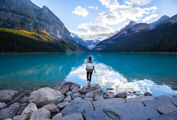 Woman standing on a rock in Lake Louise at sunset. Vacation in Canadian Rockies. Banff National Park. Alberta. Canada. - obrazy, fototapety, plakaty