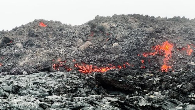 Panorama of steaming black lava rocks. Red hot molten lava flowing through streams on slope. Lava flow on Big Island in Hawaii, USA shot on smartphone camera. Volcano eruption on Mauna Loa mountain