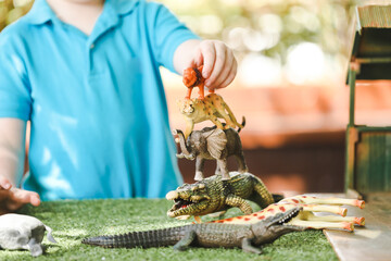 Preschool child playing with jungle animal toy set outdoors at kindergarten