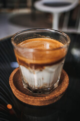 Close up dirty coffee in transparent glass served on black tray in the cafe.