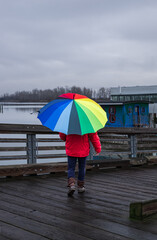Woman under rainbow umbrella. Person walking with colorful umbrella on the pier at rainy day.