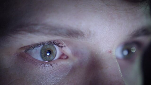 Man scrolling on his phone in a dark environment. Closeup of his eyes. Flickering lights.