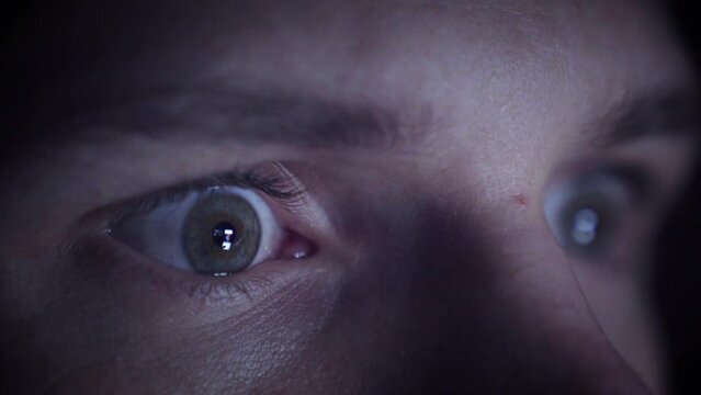 Man scrolling on his phone in a dark environment. Closeup of his eyes. Flickering lights.