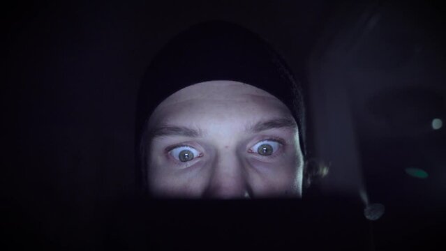 Man obsessed with scrolling in a dark environment. He is wearing a black hat.