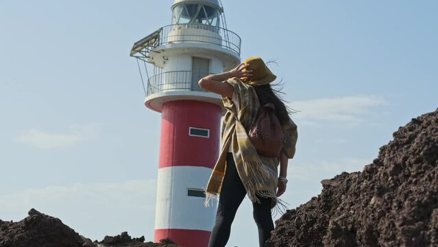 View Behind A Woman In Bohemian Hiking Outfit Facing Punta De Teno Lighthouse On A Windy Day In Tenerife, Spain. low angle, slowmo