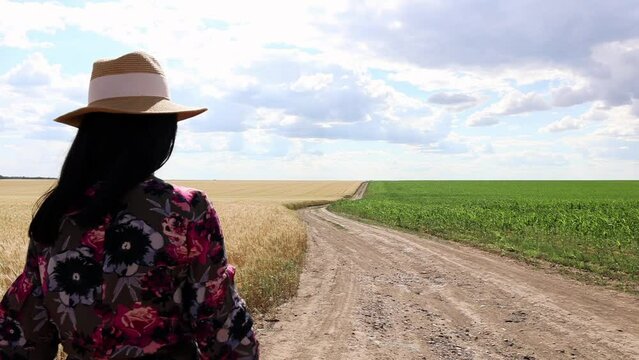 Girl In Dress And Hat Walking On Dirt Road Through Fields - medium shot