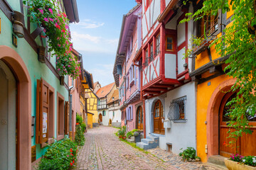 A narrow cobblestone alley of colorful half timber buildings in the medieval Alsatian village of Eguisheim, France.