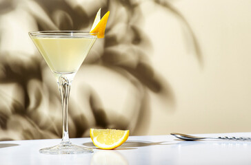 Vesper, classic alcoholic cocktail drink with dry gin, vodka, aperitif, lemon zest and ice. Light beige background, hard light, shadow pattern - obrazy, fototapety, plakaty