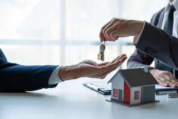 Asian young businessman, insurance sales agent handing keys to the client after signing a contract for the purchase or renting the house on the desk in new location, moving concept new beginning.