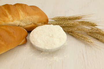 Homemade fresh bread with wheat ear on white wood table.