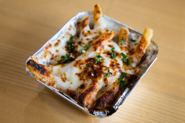 a metal take out container with baked Greek french fries loaded with melted mozzarella cheese, Greek seasoning, feta cheese, and parsley
