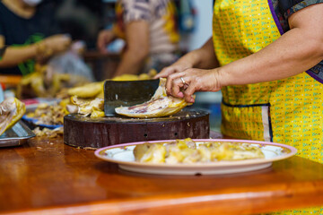 Focus on Asian chefs chopping boiled chicken on wooden chopping boards with large knife and serving on plates. Yummy and delicious food in Asia
