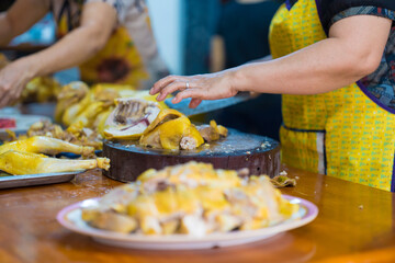 Focus on Asian chefs chopping boiled chicken on wooden chopping boards with large knife and serving on plates. Yummy and delicious food in Asia